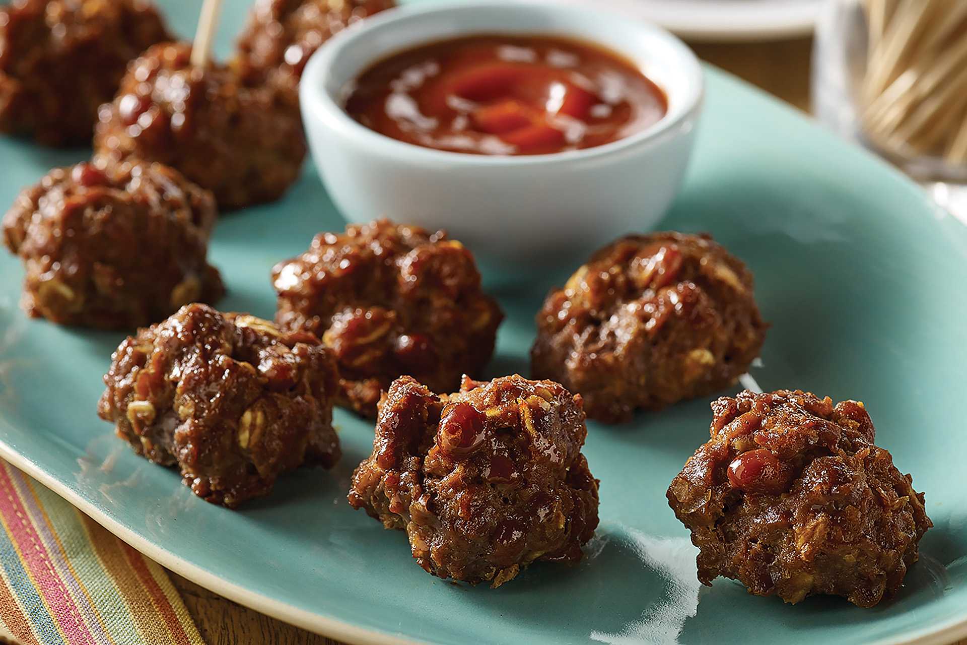 Close-up of nine honey chipotle ground sirloin meatballs with a cup of dipping sauce on a white platter