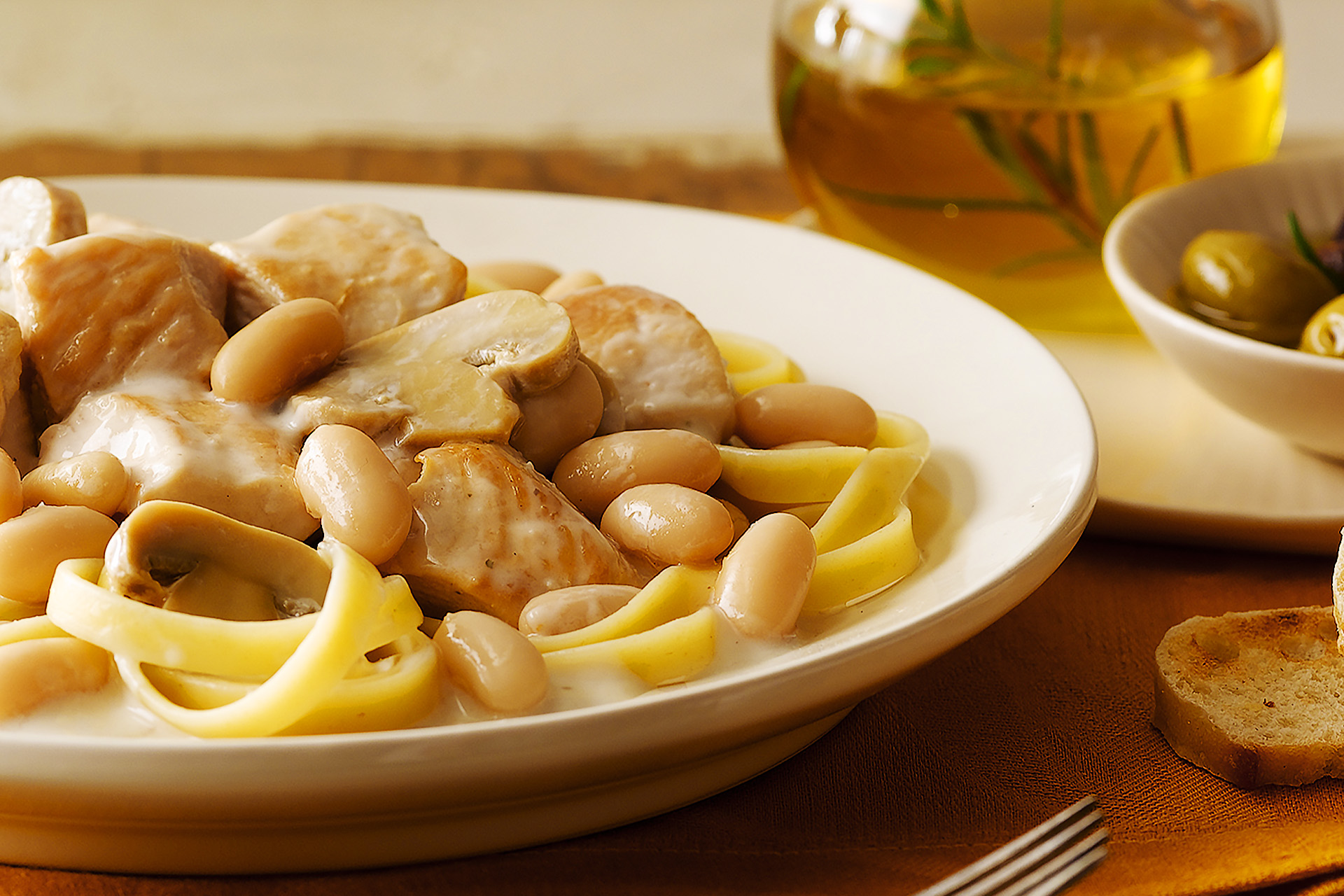 Creamy Tuscan Chicken and Mushrooms with cannellini beans over past on white plate