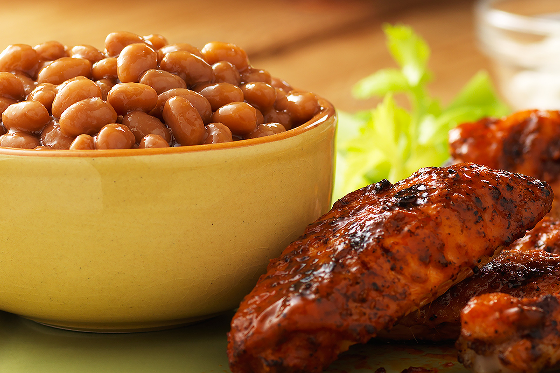 Grilled buffalo wings next to a yellow bowl of baked beans