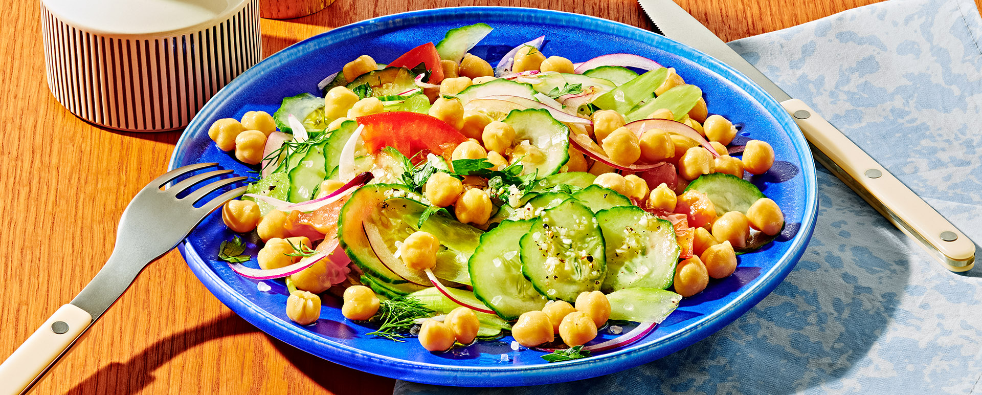 Salad with pickles, garbanzo beans, red onion and herbs in a blue bowl