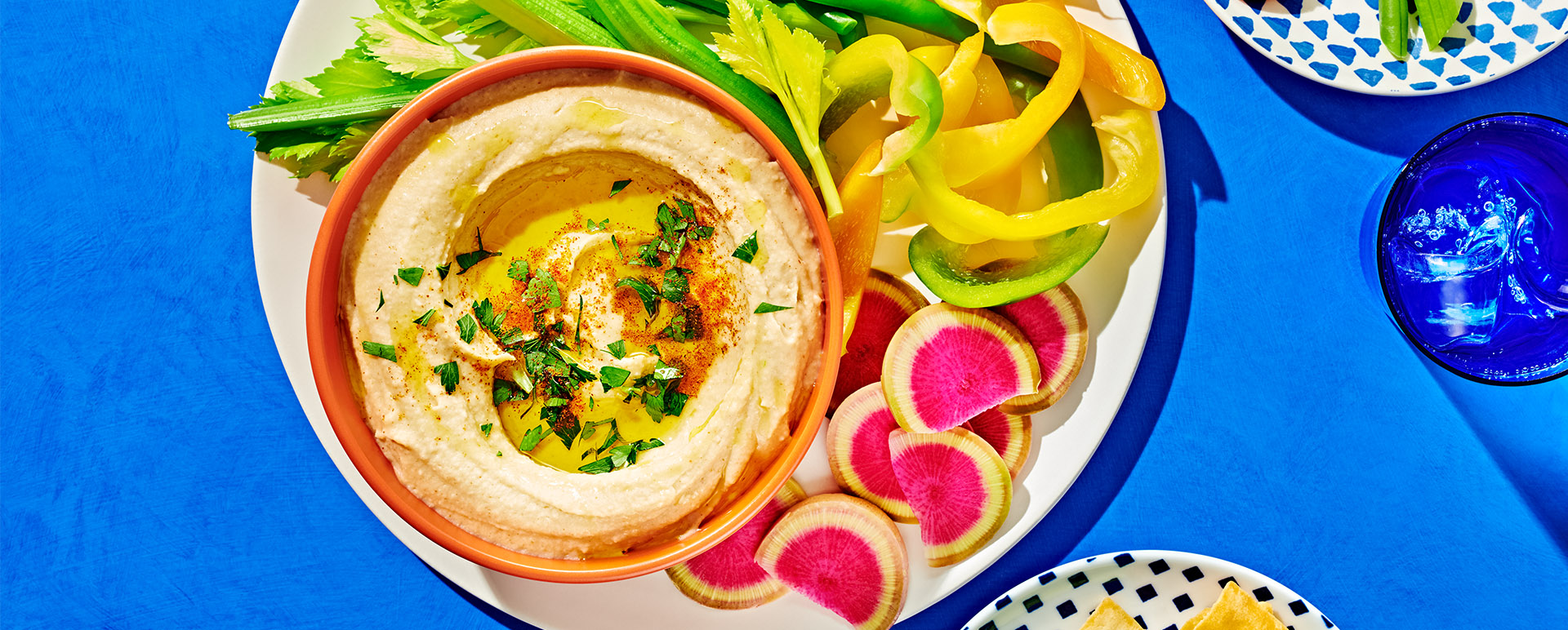 Close-up of hummus with olive oil and fresh herbs in an orange bowl